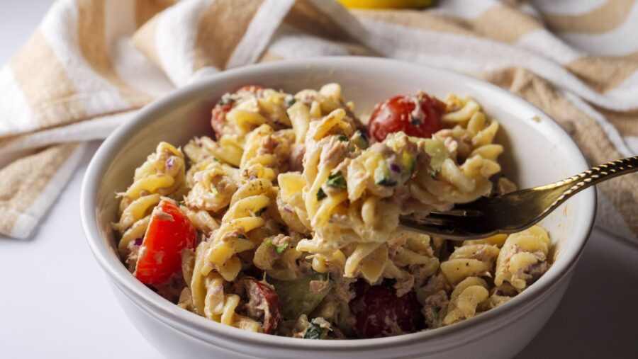 Creamy and easy tuna pasta salad with tomatoes and herbs in a white bowl.