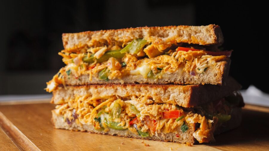 Grilled chicken sandwich with veggies and cheese on wood board.