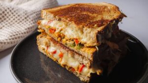 Pan-fried chicken cheese sandwich with veggies on a black plate.