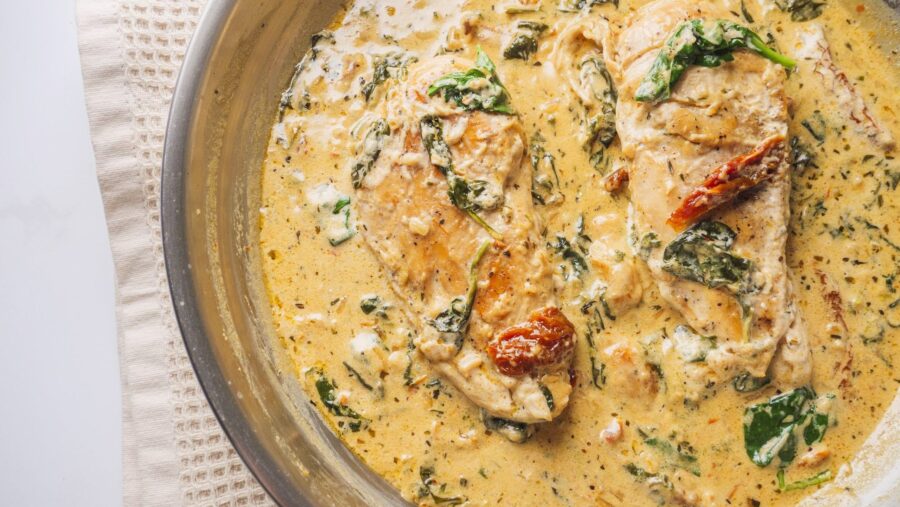 Creamy Tuscan chicken in skillet with spinach and sun-dried tomatoes.