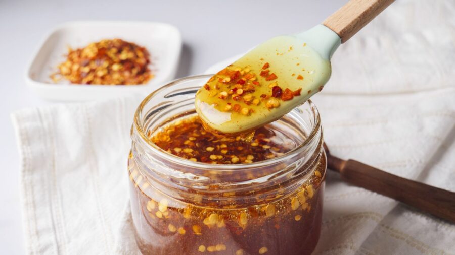 A jar of spicy chili-infused honey sauce with a spoonful being scooped.