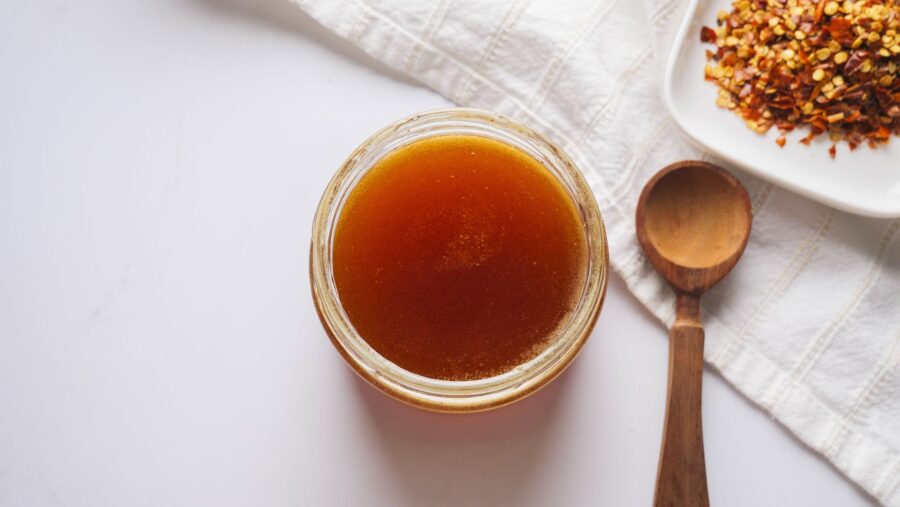Jar of spicy honey with wooden spoon and chili flakes.