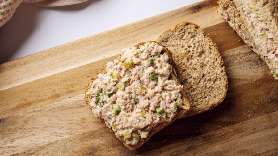 Tuna salad sandwich on whole grain bread on wooden board.