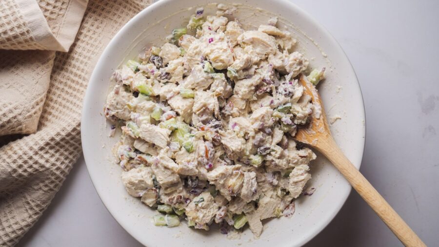Classic chicken salad with a wooden spoon in a white bowl.