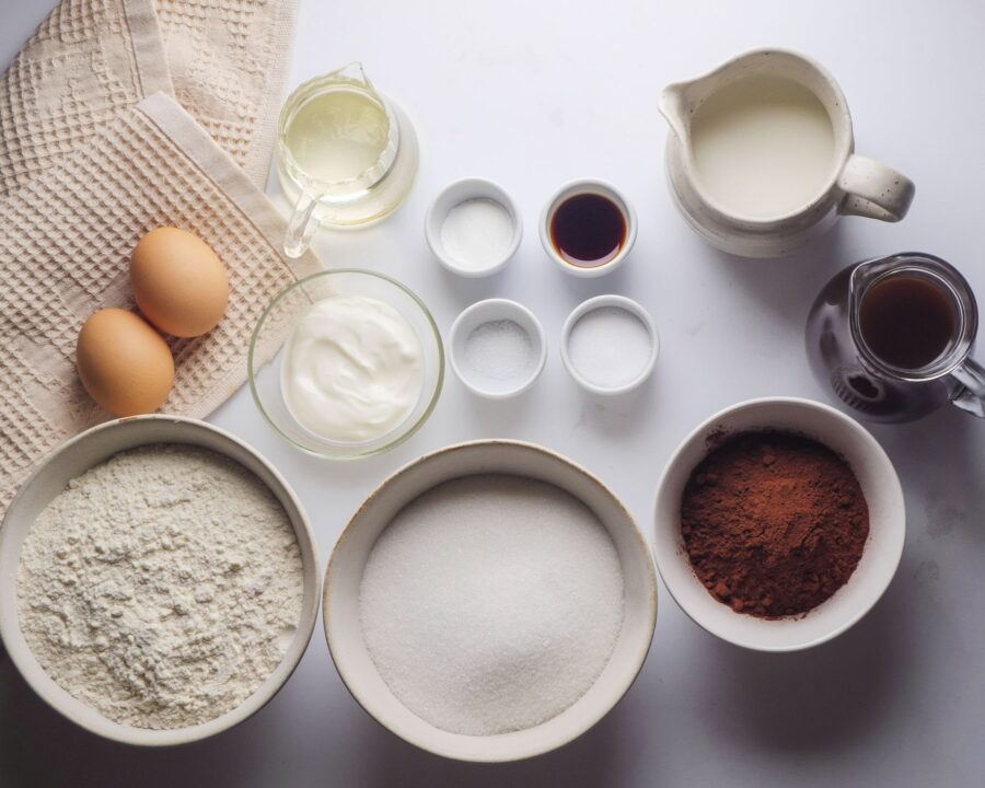 Baking ingredients on table: eggs, flour, cocoa, milk, and more.