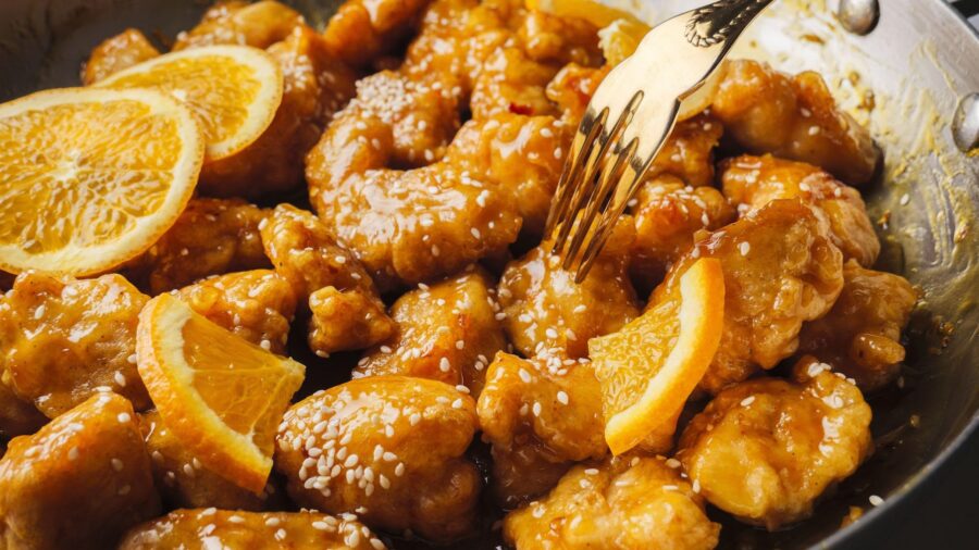 Orange chicken with sesame seeds and citrus slices.