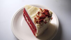 Red velvet cake slice topped with cream cheese frosting.