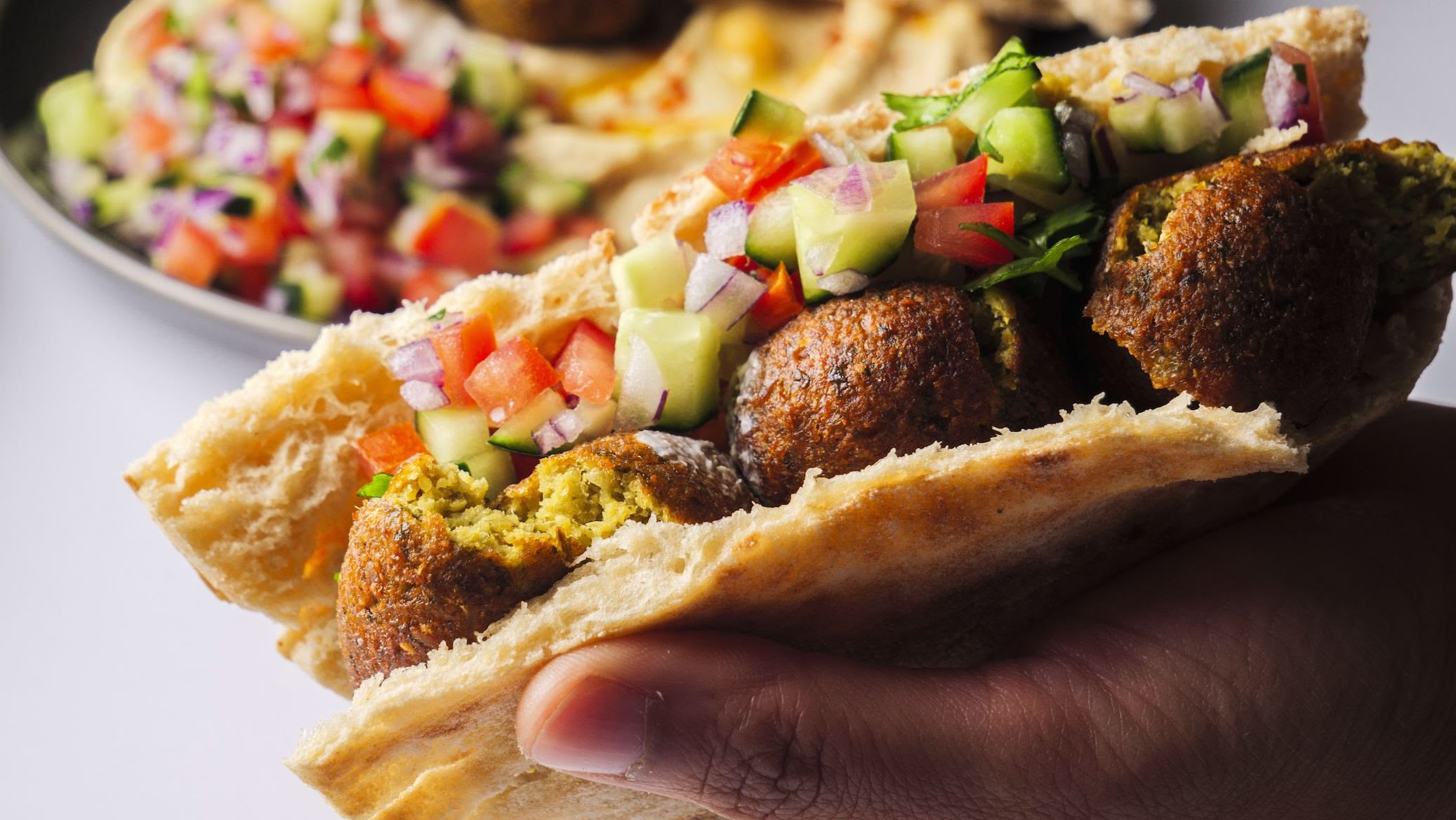 Hand holding a falafel pita with fresh veggies