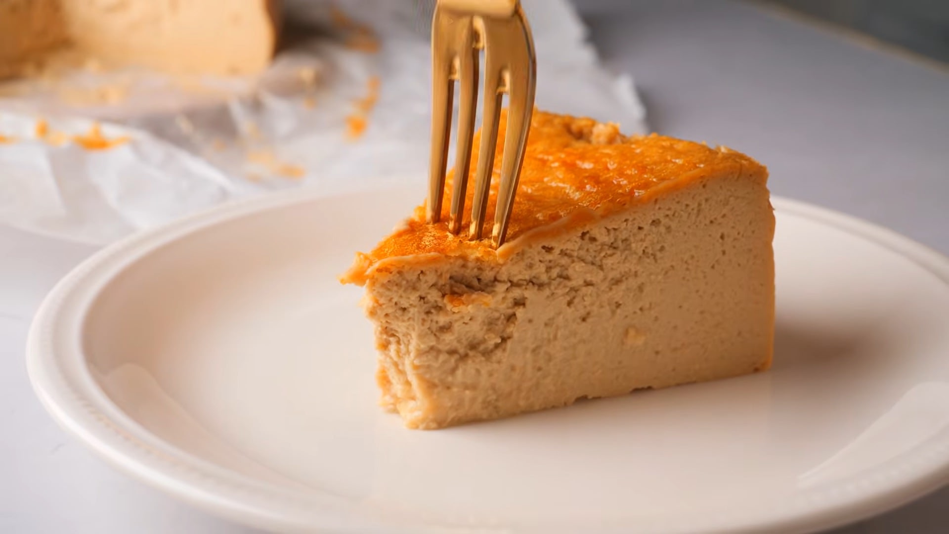 Golden fork in a coffee cheesecake slice on a white plate.