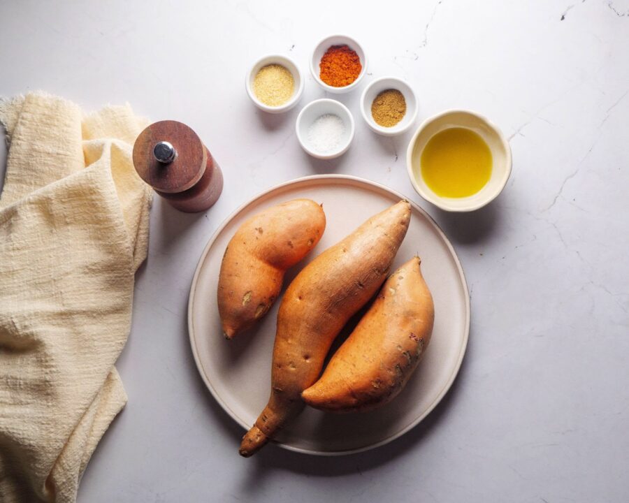 Sweet potatoes with spices and oil on a white marble background.