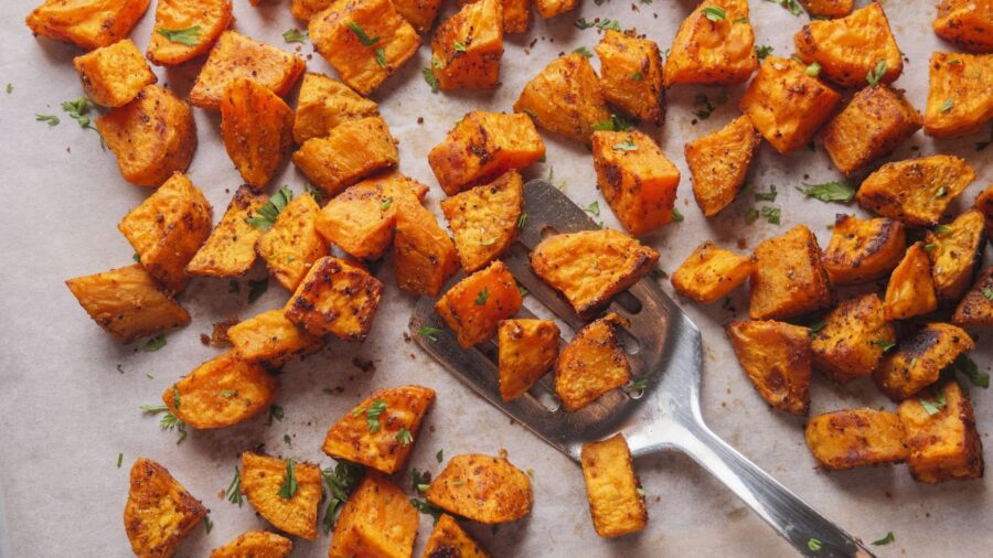 Roasted sweet potato cubes with herbs on a baking sheet.