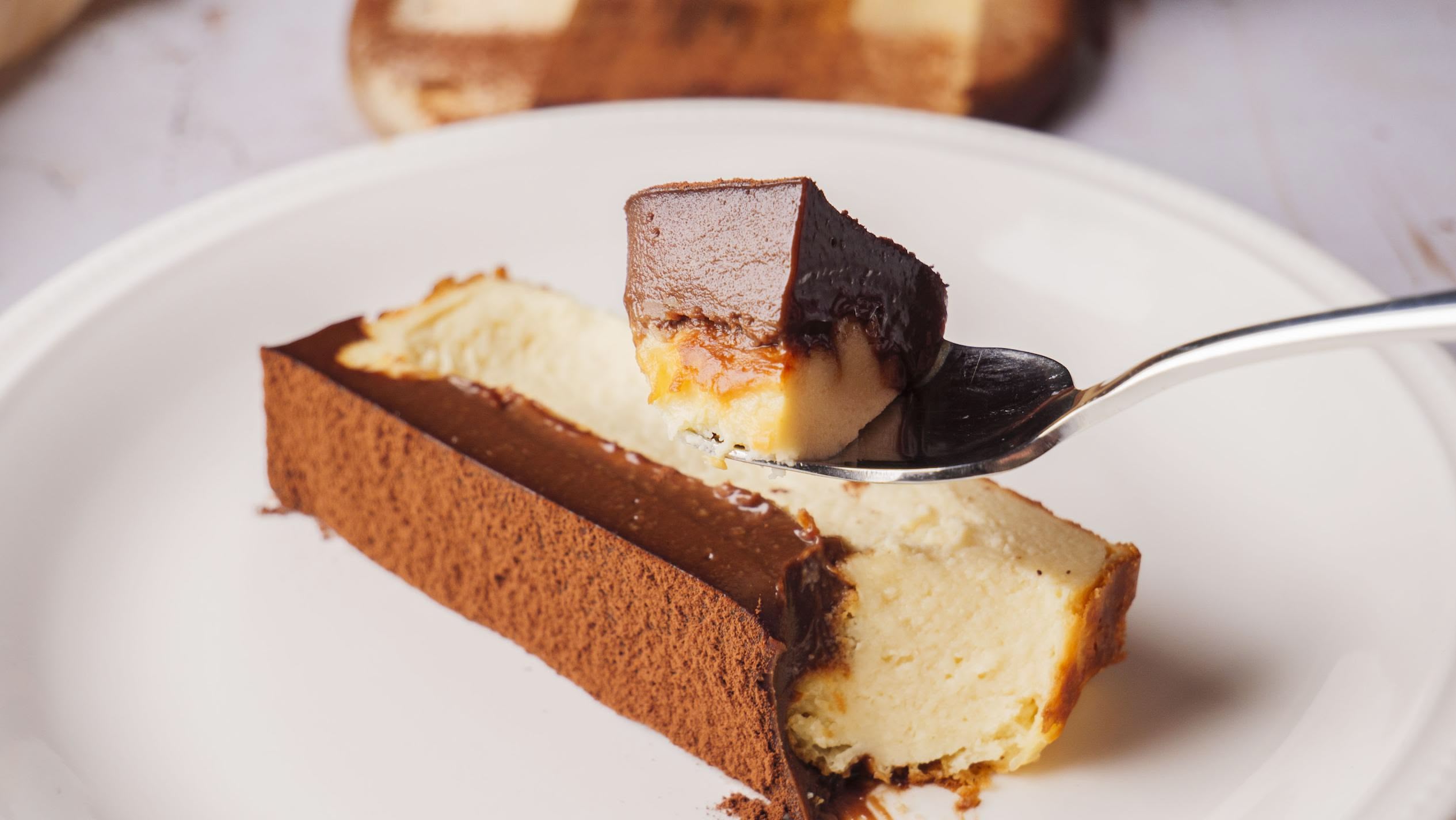Iceberg Basque Cheesecake slice on a white plate, and a little portion is on a spoon